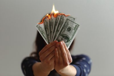 Procrastination's hidden costs. Photo of a girl burning money. Photo by JP Valery via Unsplash.