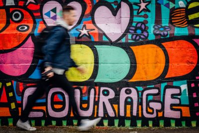 A blurry man walking in front of colorful wall. From God doesn't give us courage by J Scott McElroy